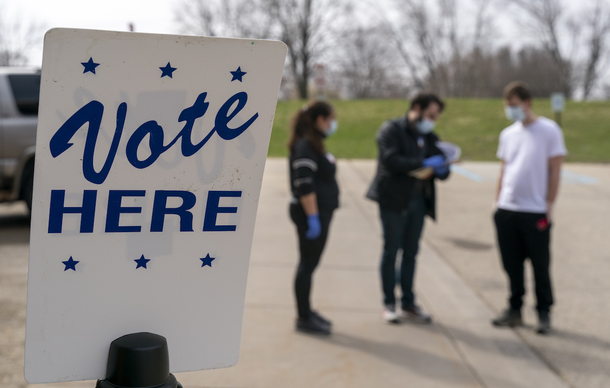People in masks stand behind a sign reading "Vote here."