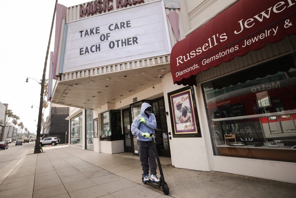 BEVERLY HILLS, CALIFORNIA - MARCH 18: A man wears gloves and a bandanna across his face while riding a scooter past a shuttered movie theater, with the message 'Take Care of Each Other' displayed on the marquee, on March 18, 2020 in Beverly Hills, California. The city of Beverly Hills mandated the closure of ‘non-essential’ stores, including the famous retailers on Rodeo Drive, starting today in response to the COVID-19 pandemic. (Photo by Mario Tama/Getty Images)