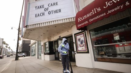 BEVERLY HILLS, CALIFORNIA - MARCH 18: A man wears gloves and a bandanna across his face while riding a scooter past a shuttered movie theater, with the message 'Take Care of Each Other' displayed on the marquee, on March 18, 2020 in Beverly Hills, California. The city of Beverly Hills mandated the closure of ‘non-essential’ stores, including the famous retailers on Rodeo Drive, starting today in response to the COVID-19 pandemic. (Photo by Mario Tama/Getty Images)