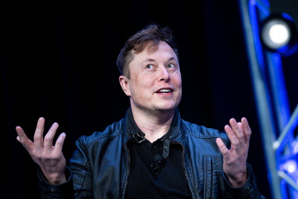 Elon Musk speaks and gestures in front of a black background