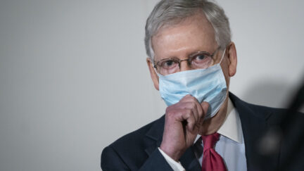 Mitch McConnell tugs at his face mask.
