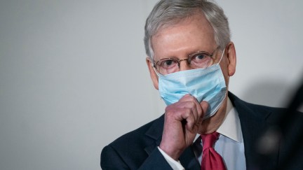 Mitch McConnell tugs at his face mask.