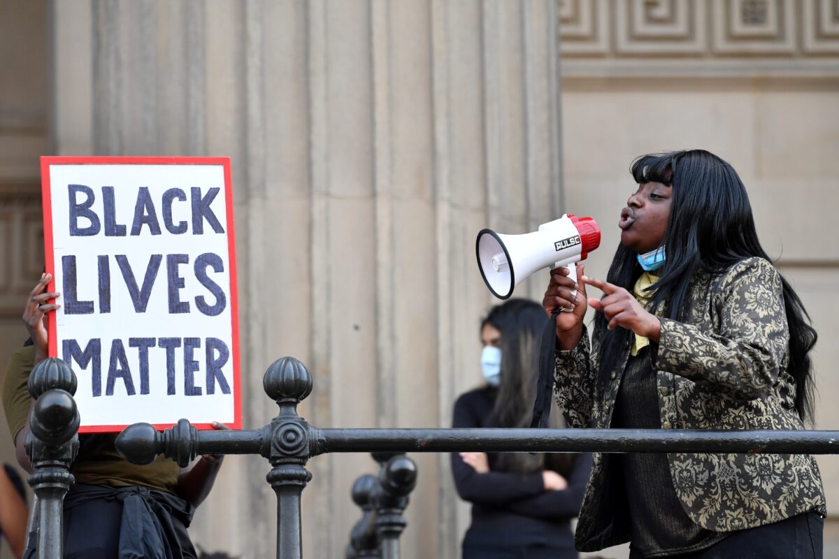 A protester addresses others through a megaphone as another holds a placard with the lettering reading 'Black lives matter' in Liverpool, northwest England, on June 2, 2020, during a demonstration after George Floyd, an unarmed black man, died after a police officer knelt on his neck during an arrest in Minneapolis, USA. - The city of Liverpool lit up their civic buildings in memory of George Floyd on June 2 the death of whom in Minneapolis while in police custody has sparked days of unrest in the US city and beyond. (Photo by Paul ELLIS / AFP) (Photo by PAUL ELLIS/AFP via Getty Images)