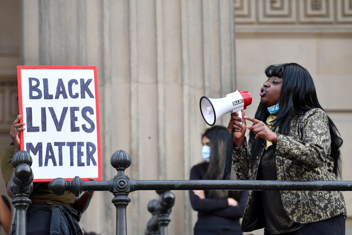 A protester addresses others through a megaphone as another holds a placard with the lettering reading 'Black lives matter' in Liverpool, northwest England, on June 2, 2020, during a demonstration after George Floyd, an unarmed black man, died after a police officer knelt on his neck during an arrest in Minneapolis, USA. - The city of Liverpool lit up their civic buildings in memory of George Floyd on June 2 the death of whom in Minneapolis while in police custody has sparked days of unrest in the US city and beyond. (Photo by Paul ELLIS / AFP) (Photo by PAUL ELLIS/AFP via Getty Images)