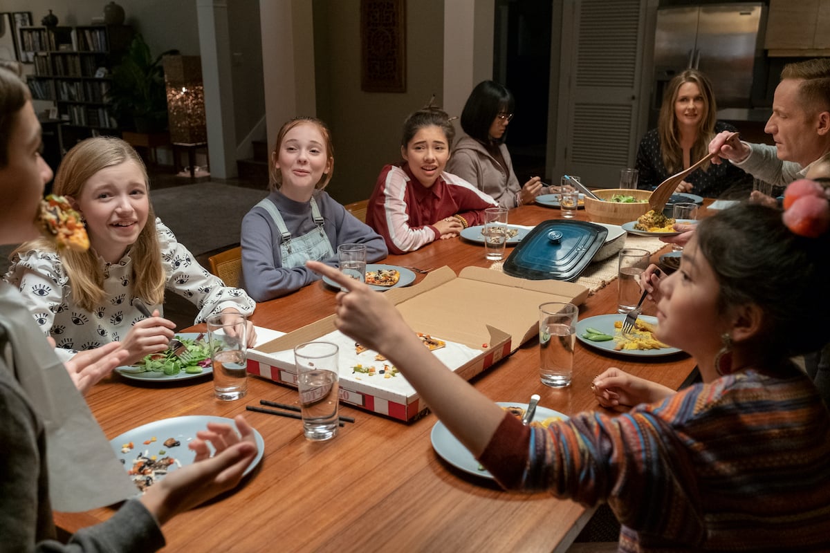 The cast of the Baby-Sitters Club gather around a dinner table.