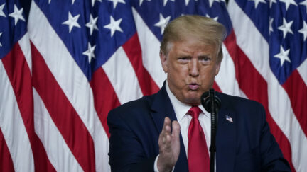 Donald Trump puffs up his cheeks in front of a row of flags.