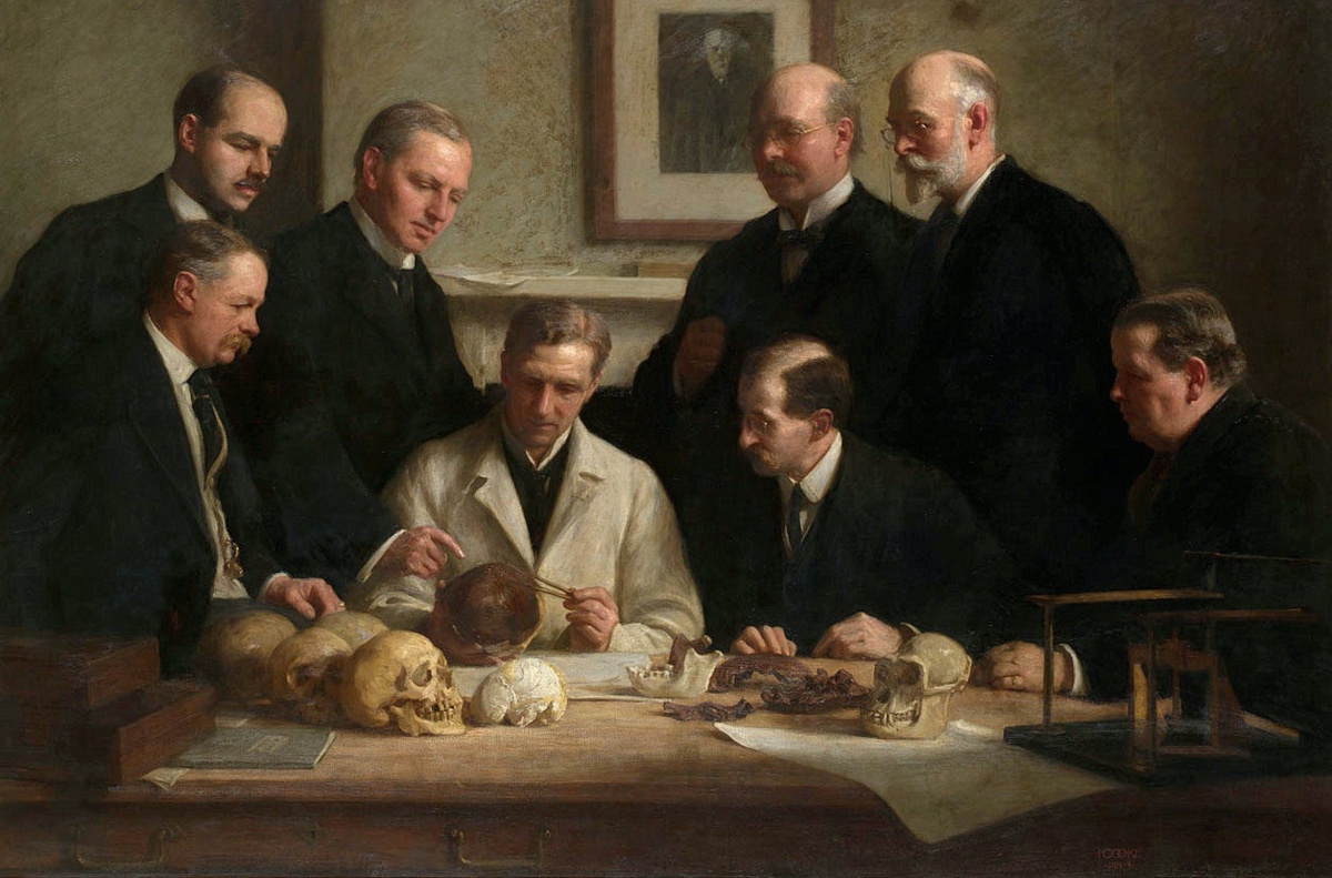 Group portrait of the Piltdown skull being examined. Back row (from left): F. O. Barlow, G. Elliot Smith, Charles Dawson, Arthur Smith Woodward. Front row: A. S. Underwood, Arthur Keith, W. P. Pycraft, and Ray Lankester. Note the portrait of Charles Darwin on the wall. Painting by John Cooke, 1915.