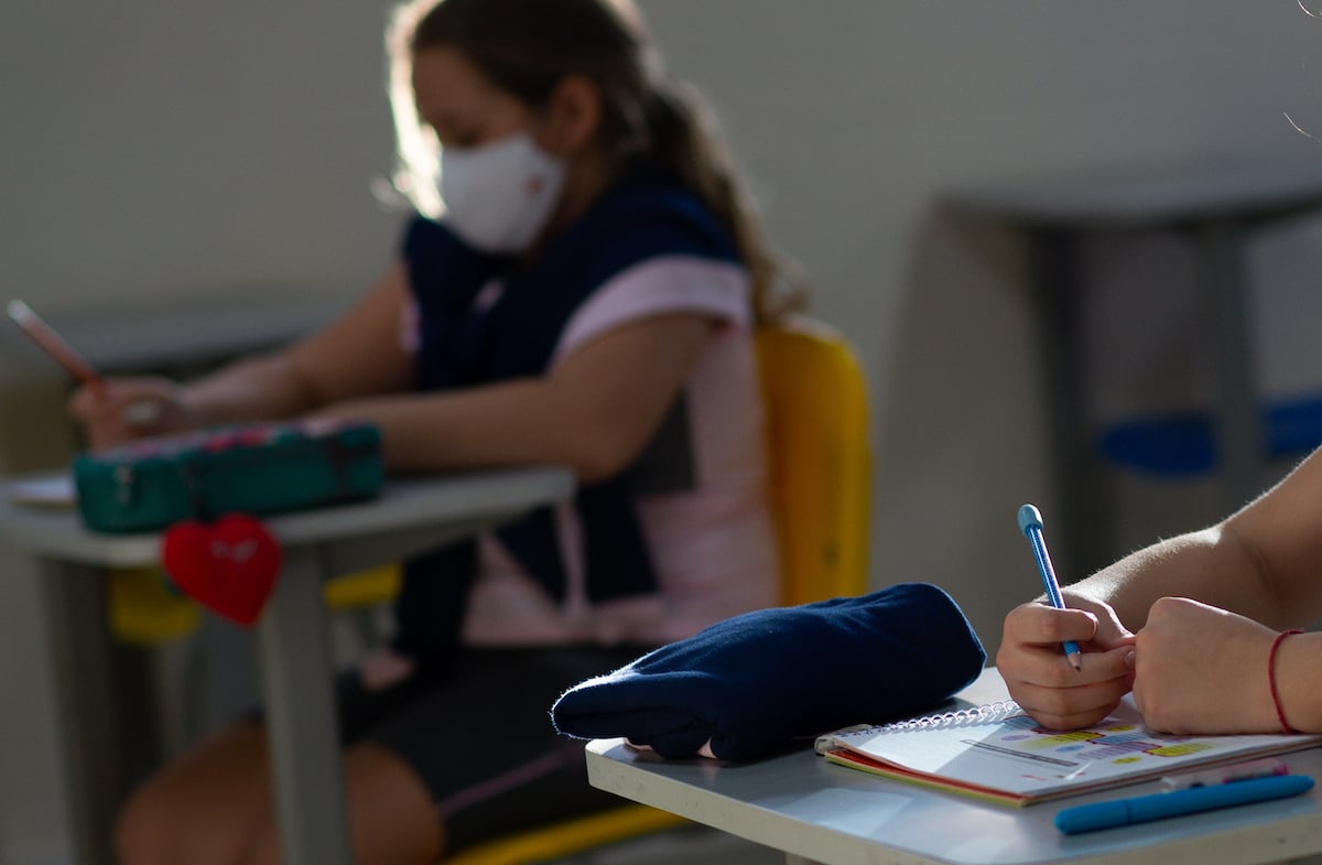 A young student wears a face mask while sitting at a school desk.