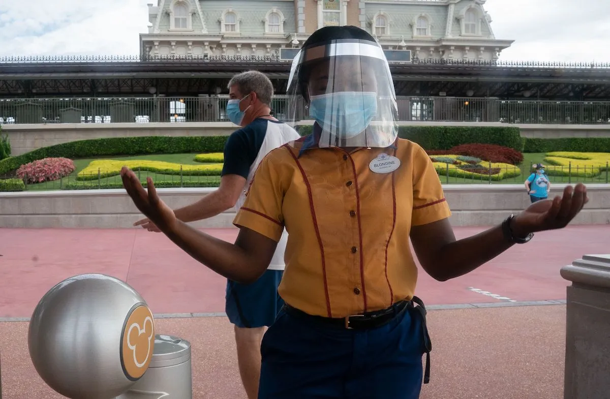An employee at Walt Disney World Resort's Magic Kingdom wears a facemask and face shield at the entrance to the park