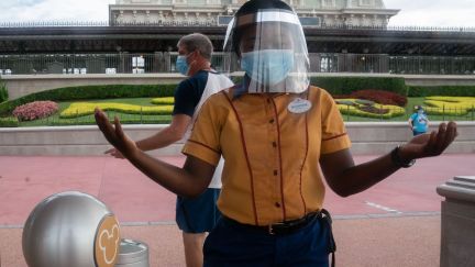 An employee at Walt Disney World Resort's Magic Kingdom wears a facemask and face shield at the entrance to the park