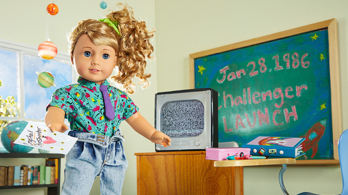 a sweet doll stands next to a black board touting the challenger launch