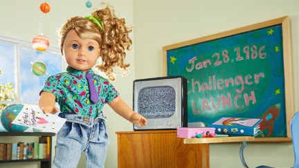 a sweet doll stands next to a black board touting the challenger launch