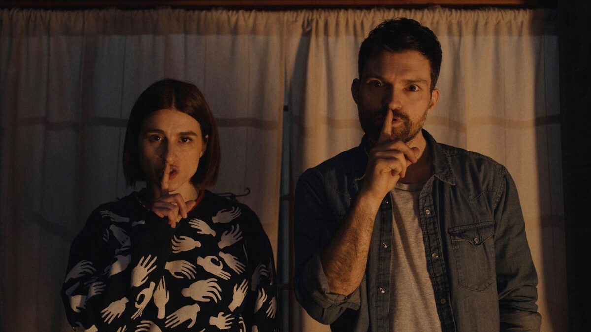 Scare Me movie still with Aya Cash and Josh Ruben making "shh" hand gestures at the camera.