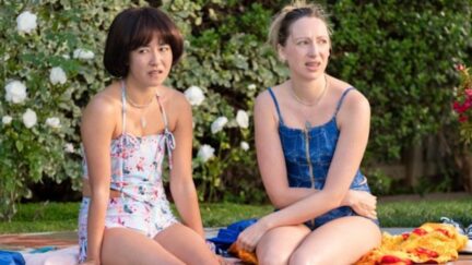 Anna and Maya from PEN15 sit in swimsuits at a pool party.
