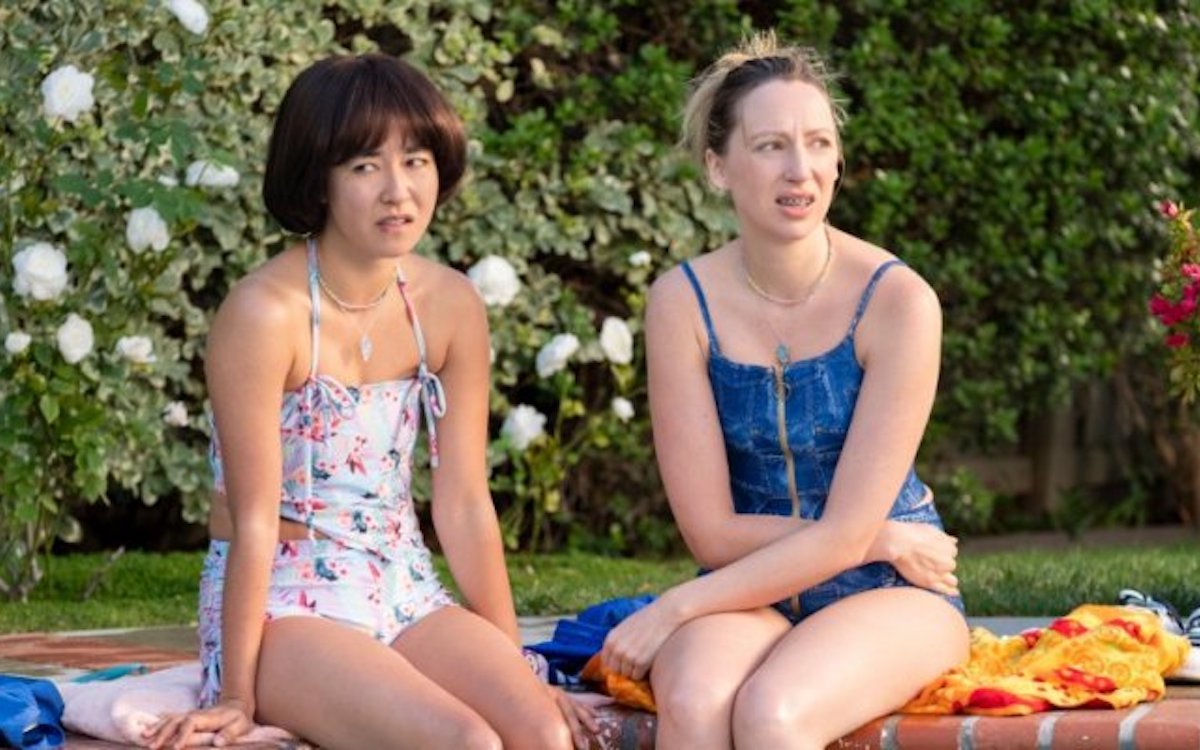 Anna and Maya from PEN15 sit in swimsuits at a pool party.