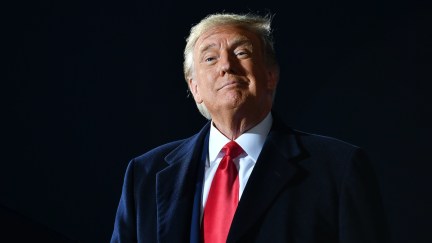 Donald Trump smirks against a black background.