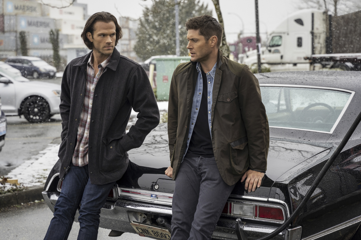 Sam and Dean lean on a car outside while having a conversation in "Supernatural"