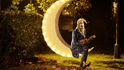 Alan Moore sitting on a crescent moon seat in The Show.