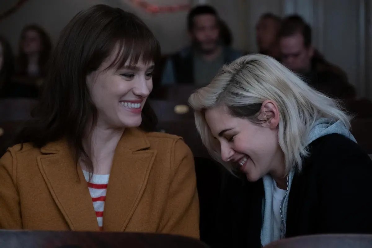 Mackenzie Davis and Kristen Stewart smile at each other in a scene from Happiest Season