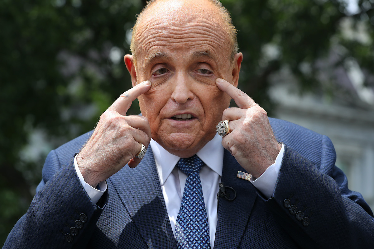 Rudy Giuliani pulls at his face while talking to reporters.