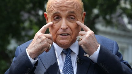 Rudy Giuliani pulls at his face while talking to reporters.