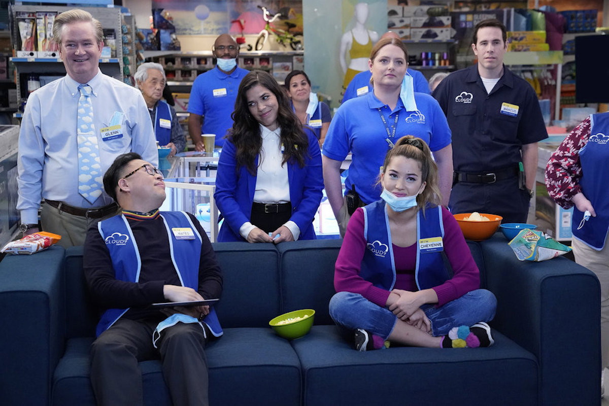 Characters from Superstore sit on and around a sofa, some in masks.