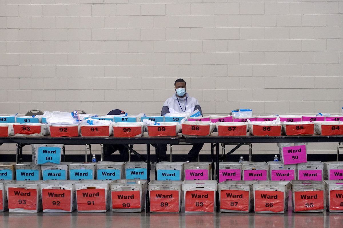 An election official sits behind a row of ballots to be recounted.