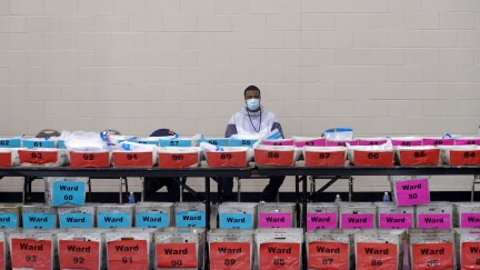 An election official sits behind a row of ballots to be recounted.