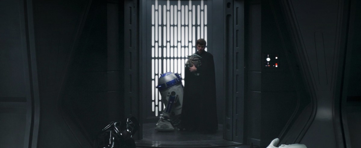 Luke Skywalker holds Grogu while standing next to R2-D2 in an elevator
