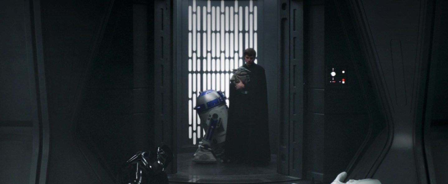 Luke Skywalker holds Grogu while standing next to R2-D2 in an elevator