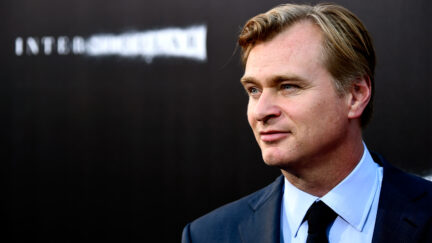 Christopher Nolan stands in front of a marketing background for Interstellar.