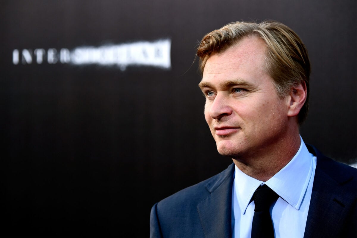 Christopher Nolan stands in front of a marketing background for Interstellar.