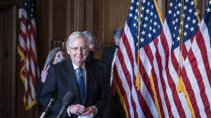 Mitch McConnell smirks as he enters for a press conference.