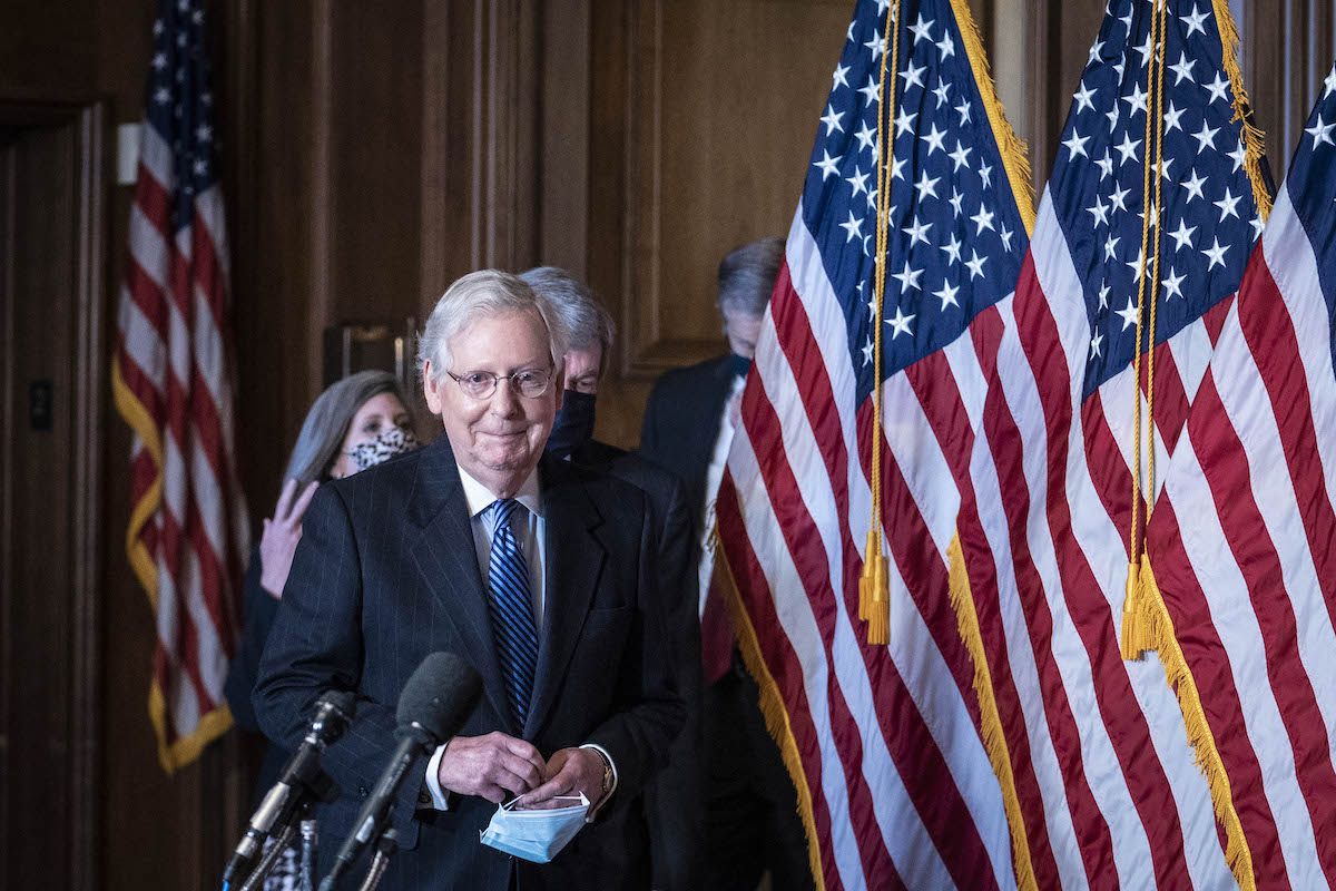 Mitch McConnell smirks as he enters for a press conference.