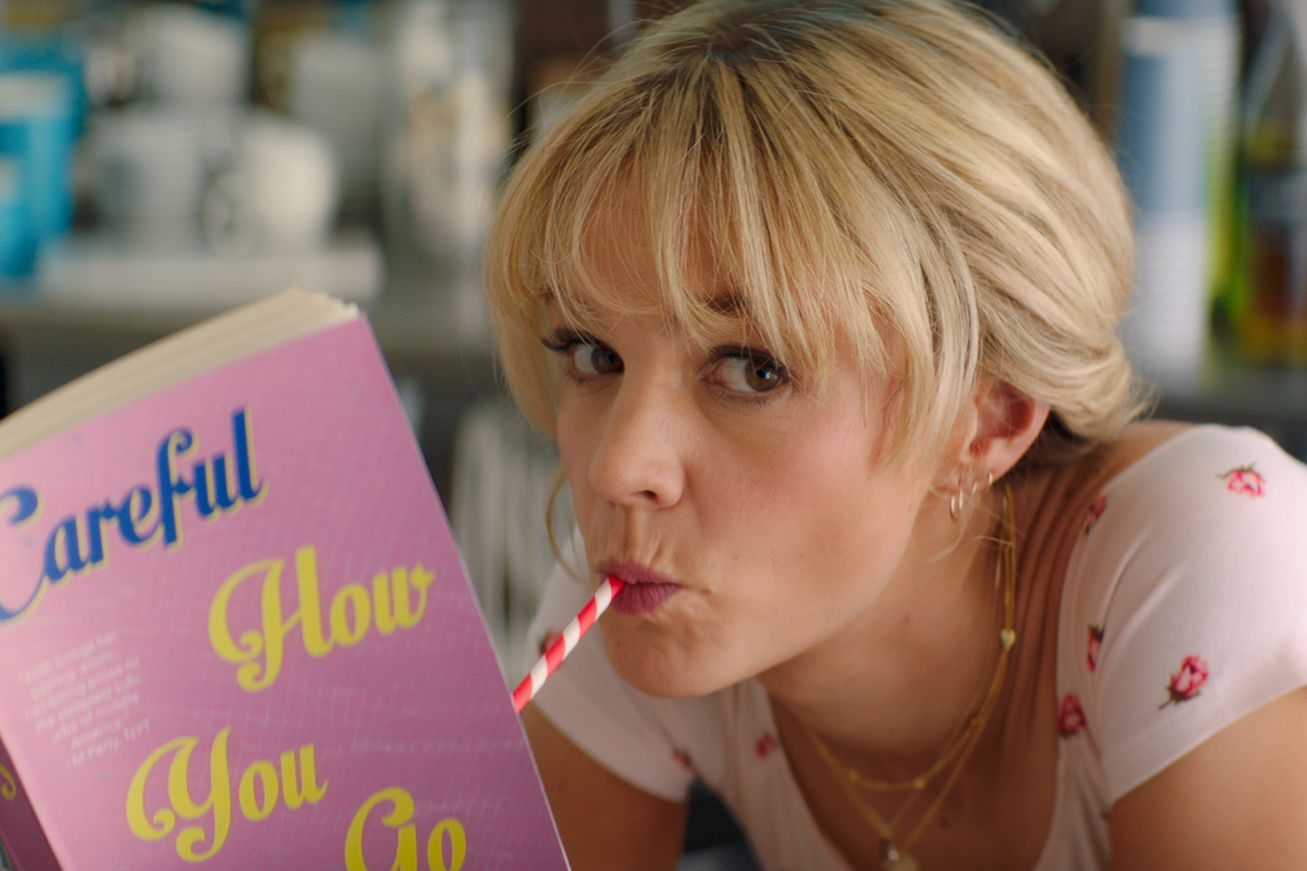 In a scene from Promising Young Woman, Cassie (Carey Mulligan) drinks from a pink straw while reading a book with a pink cover.