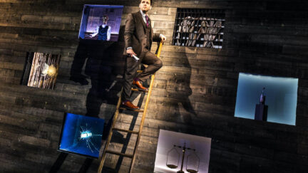 Derek DelGaudio at the top of a ladder on stage for In & Of Itself