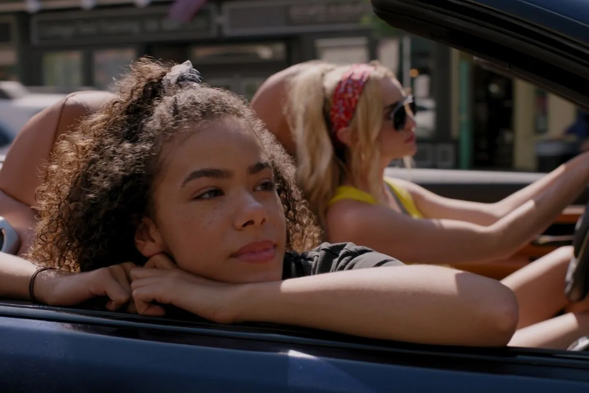A white mother and her biracial daughter drive in a drop-top car with hopeful looks on their faces.