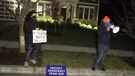 Two protesters stand outside Josh Hawley's home.