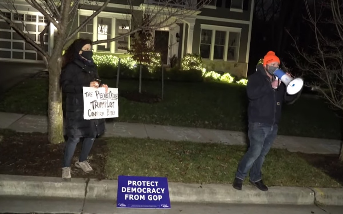 Two protesters stand outside Josh Hawley's home.