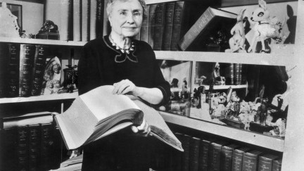 1956: Portrait of American writer, educator and advocate for the disabled Helen Keller (1880 - 1968) holding a Braille volume and surrounded by shelves containing books and decorative figurines. A childhood illness left Keller blind, deaf and mute. (Photo by Hulton Archive/Getty Images)