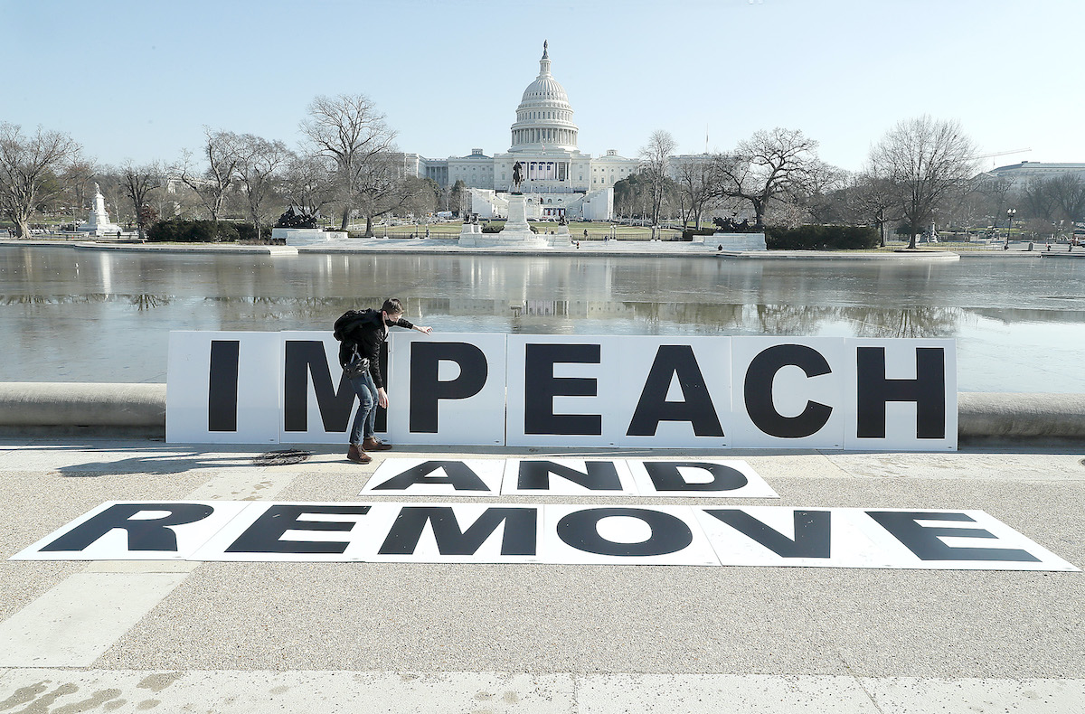 People gather at the base of the U.S. Capitol with large IMPEACH and REMOVE signs