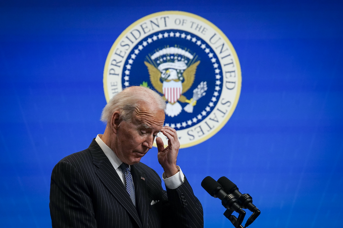 Joe Biden scratches his head in front of the presidential seal.