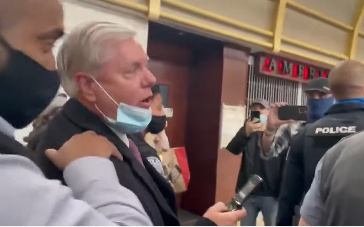 Lindsey Graham is escorted through an airport by police as people yell at him.