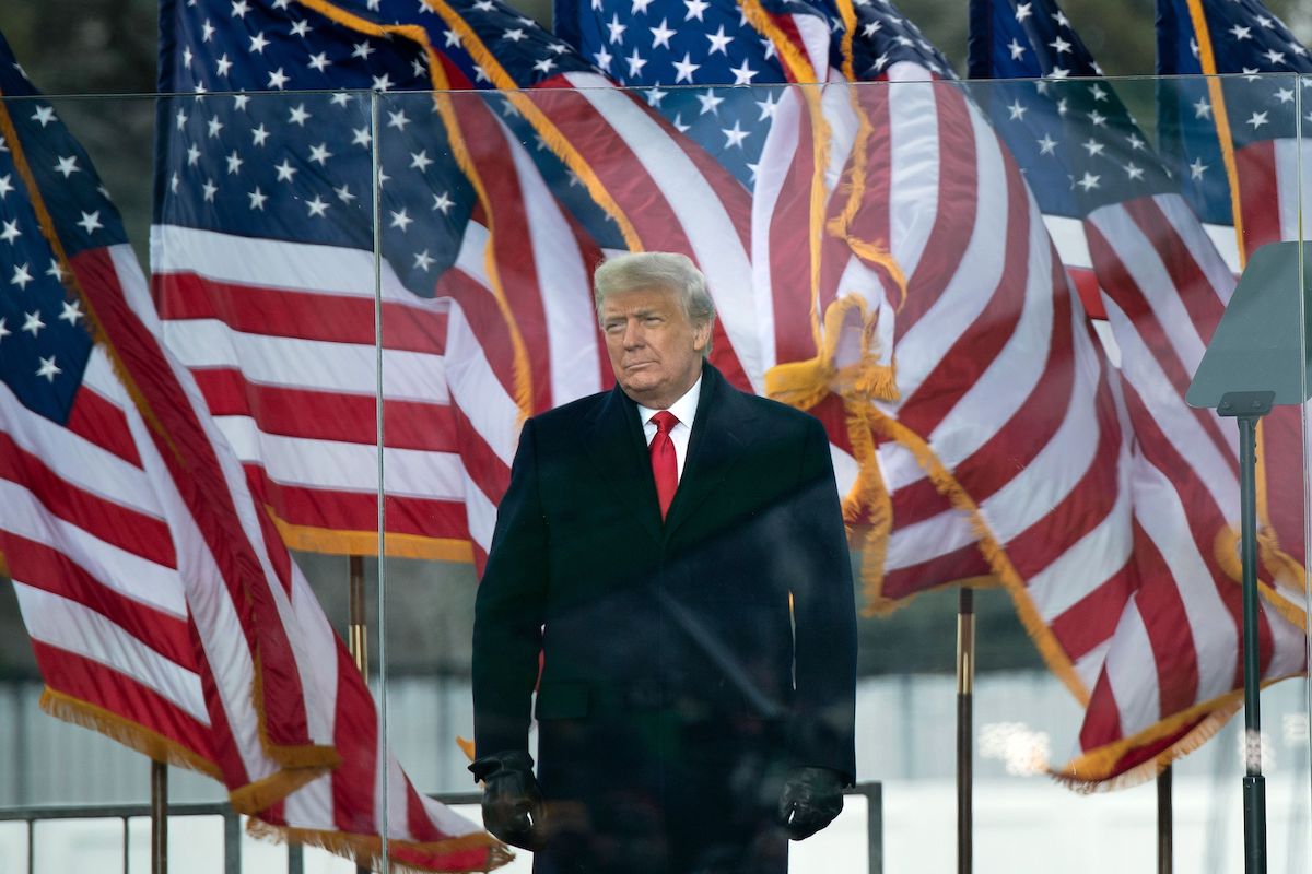 Donald Trump speaks during an outdoor rally, standing in front of American flags.