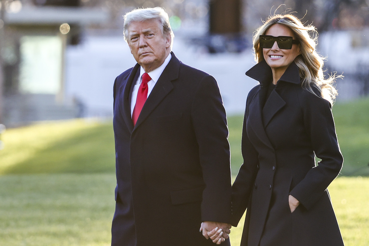 Donald and Melania Trump hold hands outdoors.