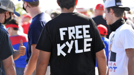 A man at a rally wears a black t-shirt shirt reading 