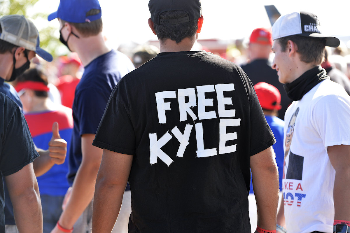 A man at a rally wears a black t-shirt shirt reading "Free Kyle" written in white tape on the back.