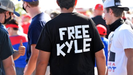 A man at a rally wears a black t-shirt shirt reading 