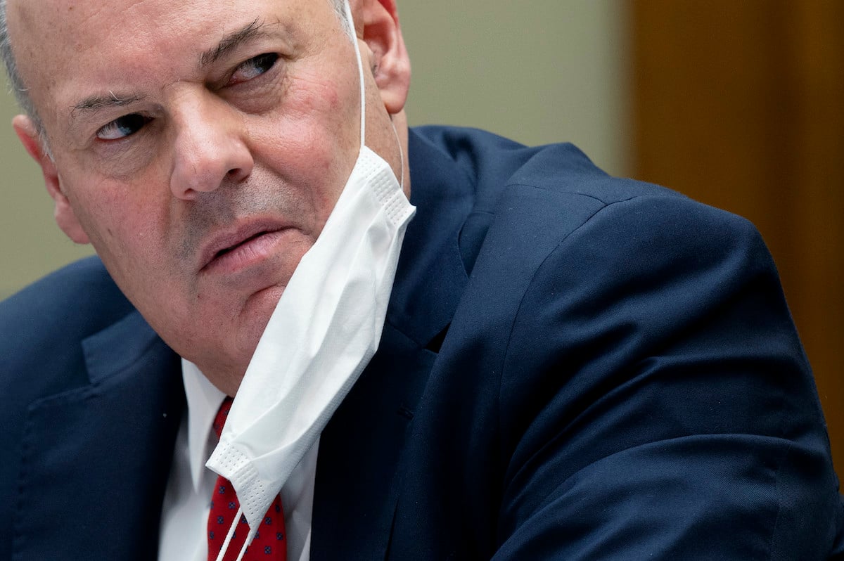 United States Postal Service Postmaster General Louis DeJoy looks angry with a mask hanging from his ear while testifying during a House Oversight and Reform Committee hearing