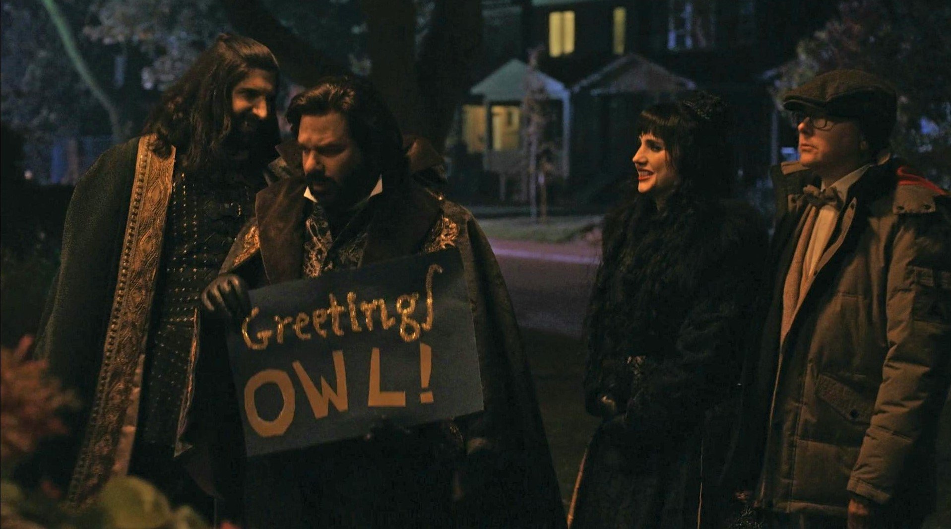 the vampires of what we do in the shadows hold a "greetings owl" sign